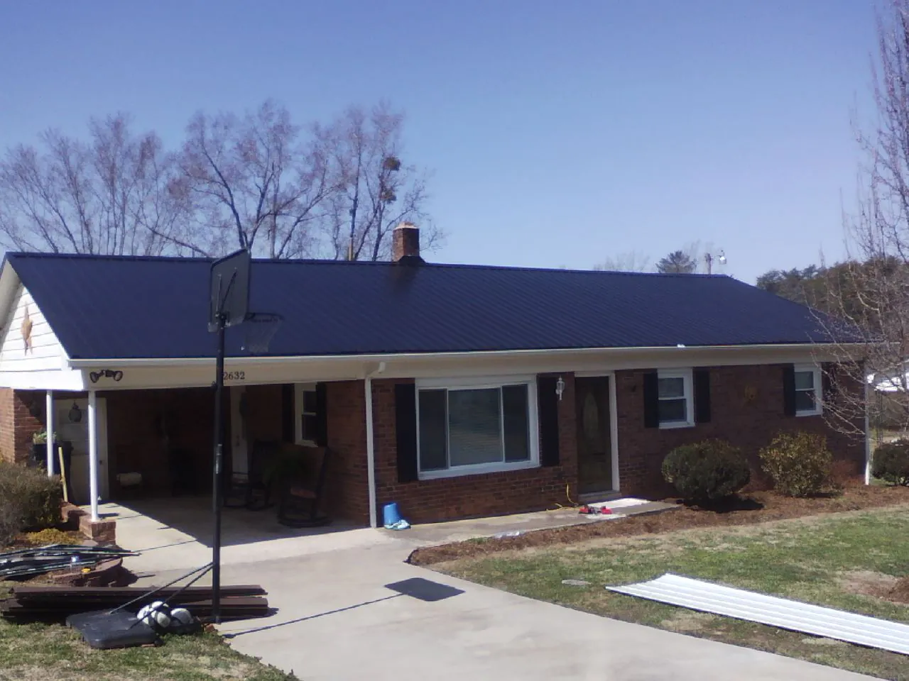 Finished dark blue metal roof on a brick ranch with a carport in Mckeesport