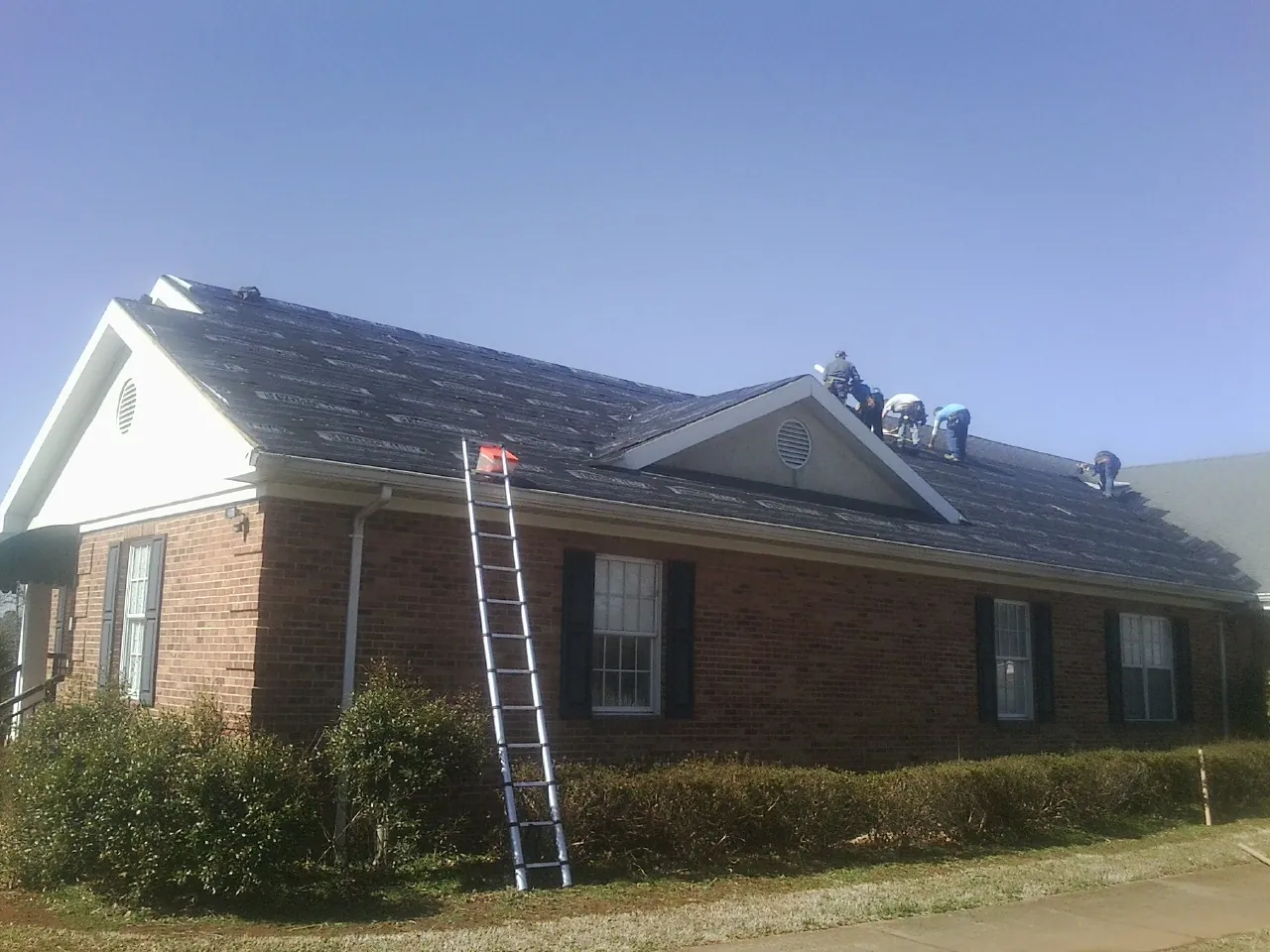 Crew tearing shingles off a brick ranch roof with a ladder set — Emergency Roof Repair work by our crew in Mckeesport