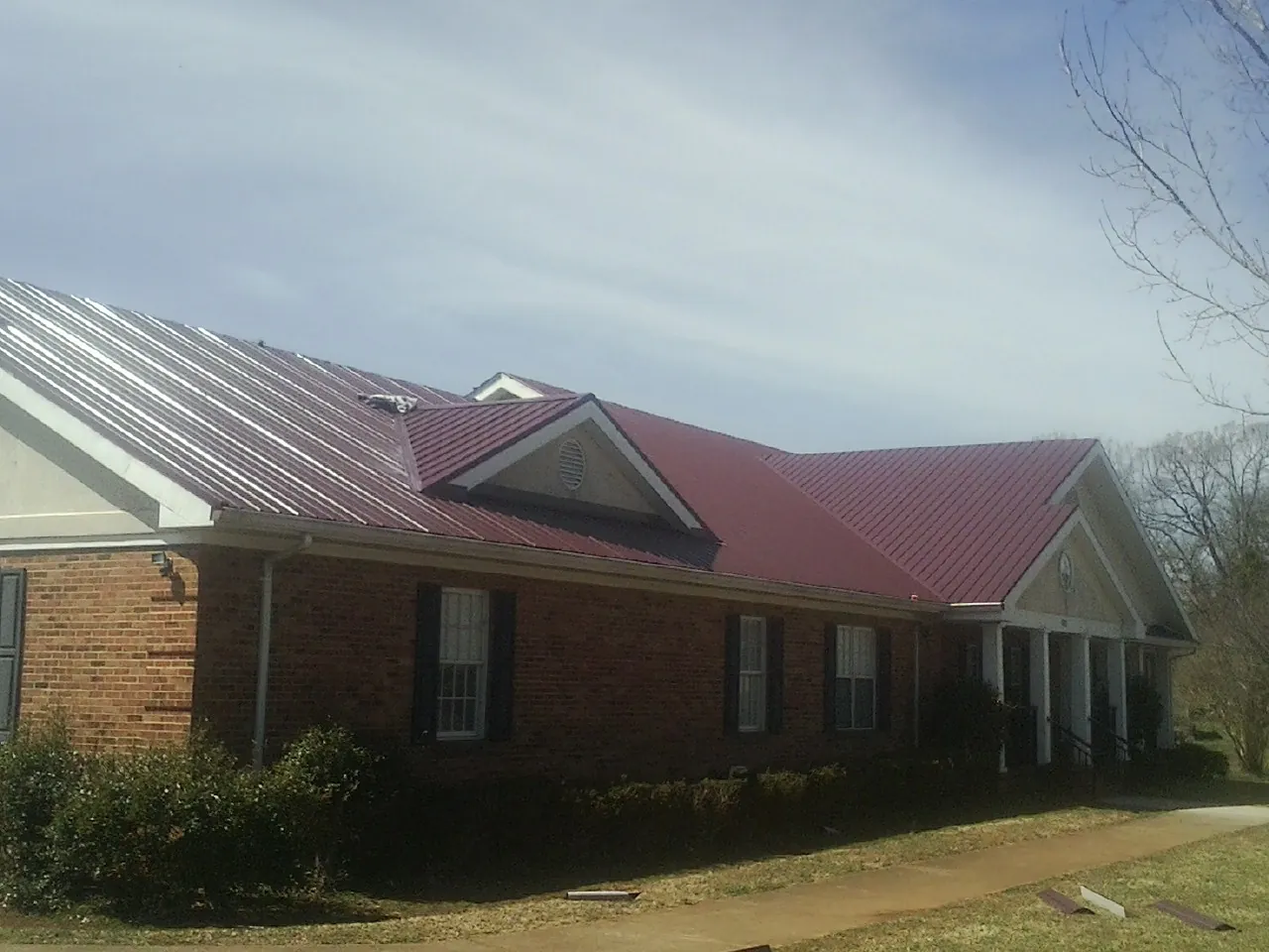 Red metal roof with gabled entries on a long brick building, from a Hail Damage Roof Repair job in Mckeesport