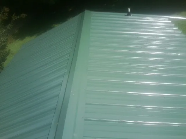 New green metal panels meeting at the ridge of a roof — Flat Roof Repair work by our crew in Mckeesport