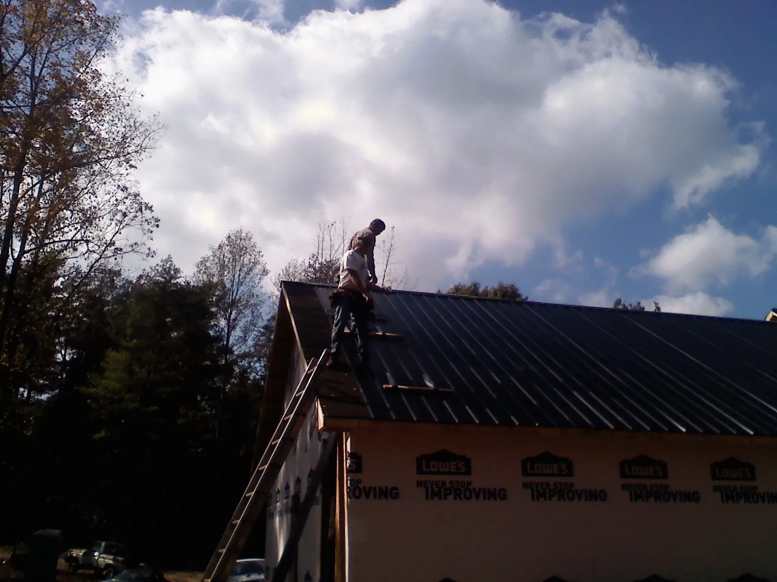 Roofer fastening dark metal panels high against a cloudy sky, from a Roof Inspection job in Mckeesport