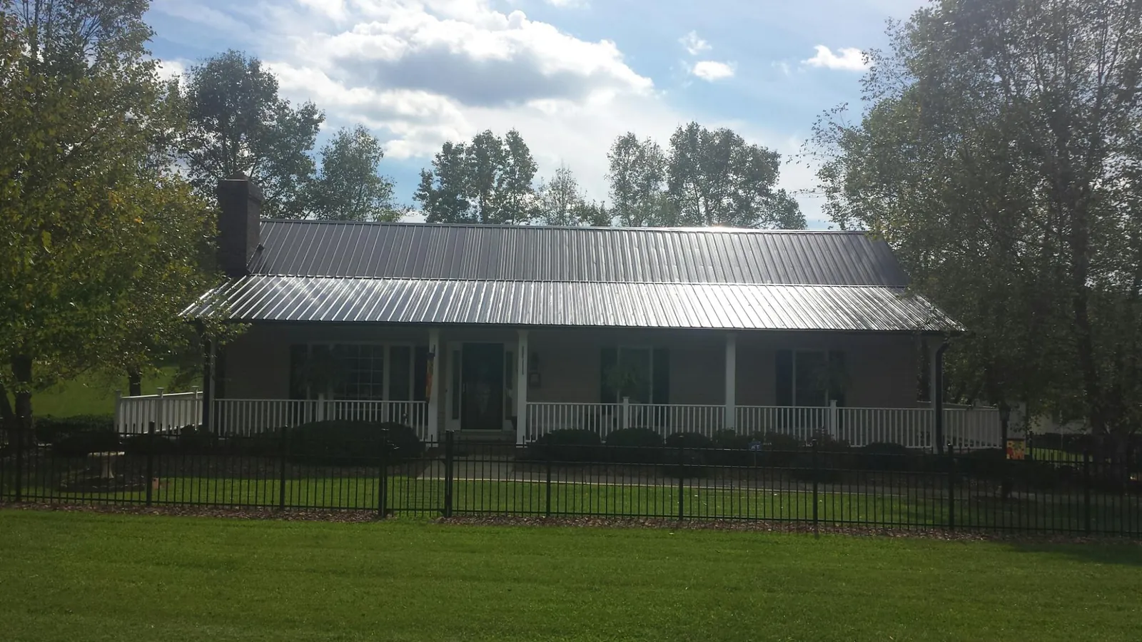 Gray metal roof on a brick ranch with a full width front porch — Gutter Guard Installation work by our crew in Mckeesport
