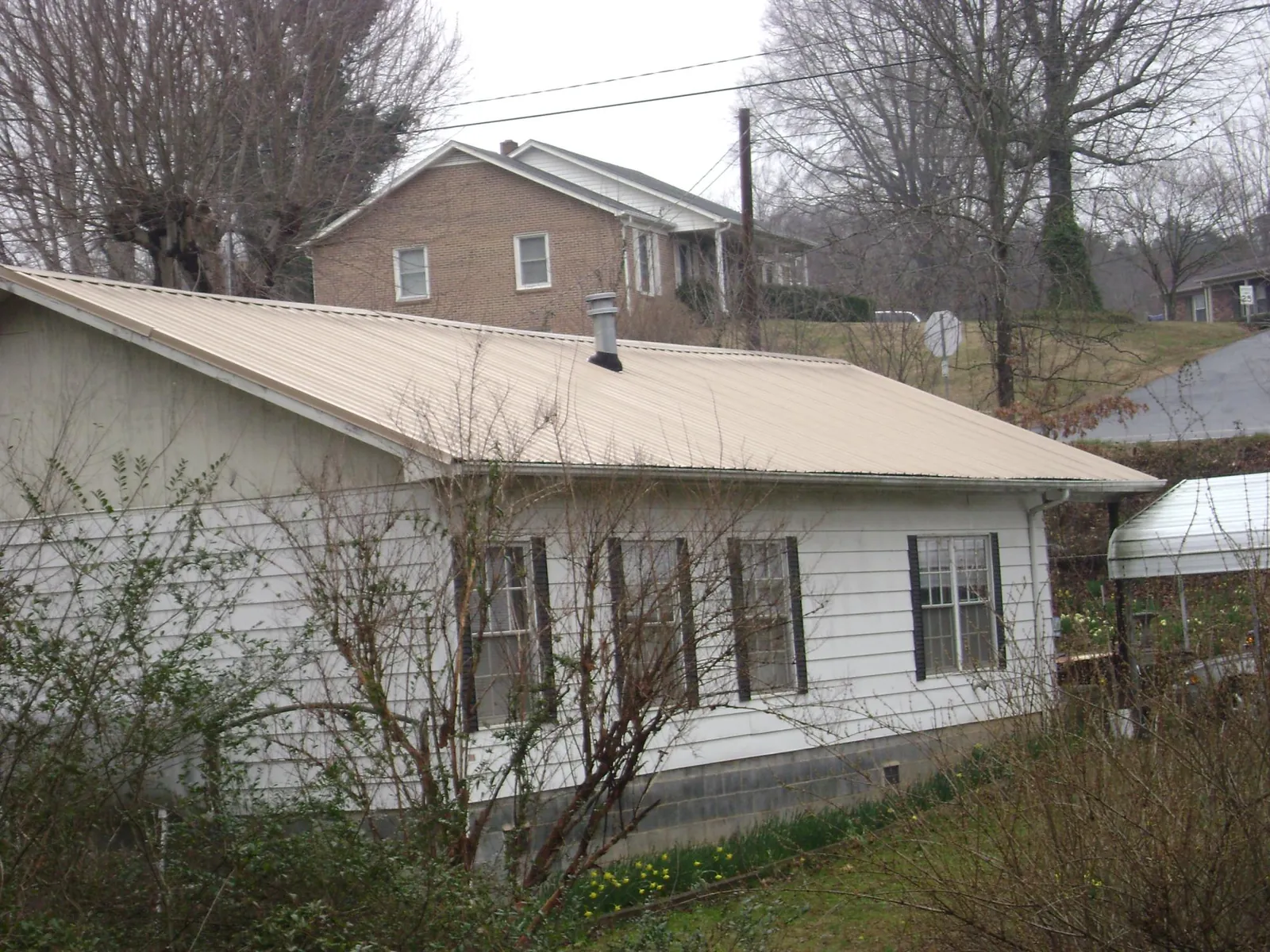Tan metal roof on a white sided house set into a hillside — Commercial Roofing by Roofing Brothers in Mckeesport